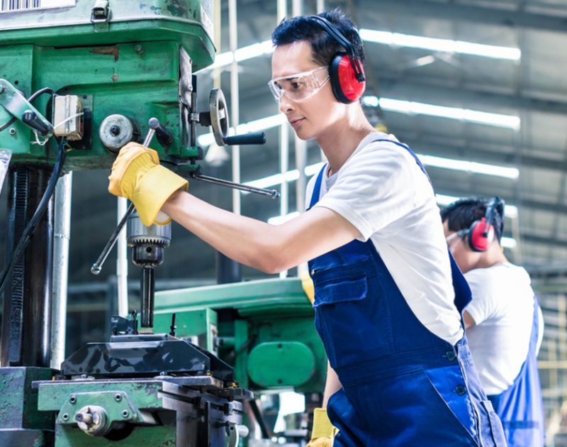 Asian worker in production plant drilling at machine on the factory floor